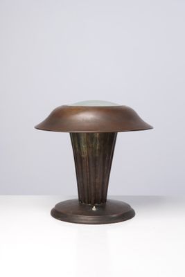 une lampe de table en bronze posée sur une surface blanche, sur fond gris