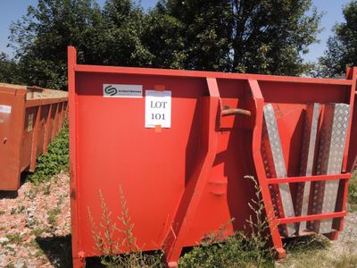 une benne rouge posée au milieu d'un champ