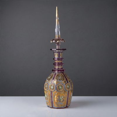 un vase violet et doré, surmonté d'un couvercle doré, posé sur une table blanche