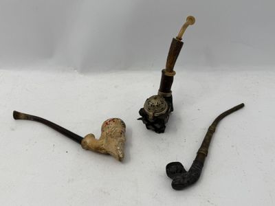 deux pipes et un porte-pipe posés sur une surface blanche