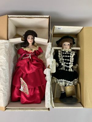 Deux poupées dans une boîte : l'une porte une robe rouge et l'autre une robe noire et blanche.