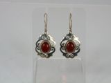 a pair of silver and red stone earrings on a clear surface
