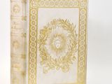 an old book with a gold and white cover on a white surface