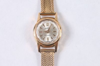 une montre-bracelet en or avec un cadran blanc sur une surface blanche