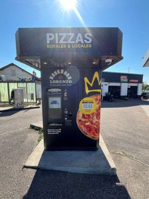 un distributeur automatique sur lequel est posée une pizza, dans un parking