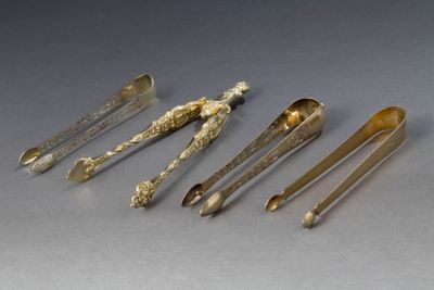 cinq cuillères en argent et un repose-cuillère sur une table