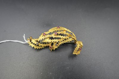 gold leaf brooch with red and blue stones on a black surface