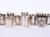 six tasses en argent et une cuillère en argent sont alignées sur une surface blanche