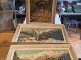 two paintings of mountains and a bridge are on display in a shop