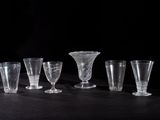 six clear glass goblets are lined up on a black table