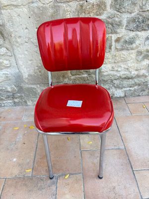 une chaise rouge avec une étiquette, posée devant un mur de pierre