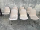 six chaises blanches sont alignées contre un mur en béton