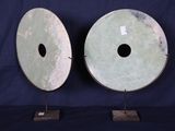 paire de grandes sculptures en forme de disques en jade vert, posées sur des socles, sur fond bleu