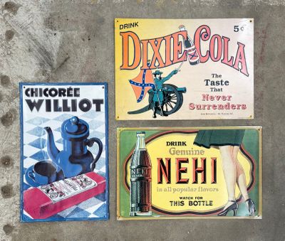 Trois enseignes publicitaires vintage différentes sont exposées sur une surface en béton
