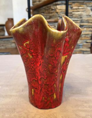 un vase rouge et doré posé sur une table devant un mur de pierre