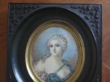 painting of a woman in a blue dress in a black frame on a wooden table
