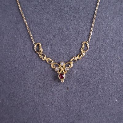 un gros plan sur un collier en or orné d'une pierre rouge