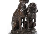 statue en bronze représentant deux chiens assis l'un à côté de l'autre sur une surface blanche