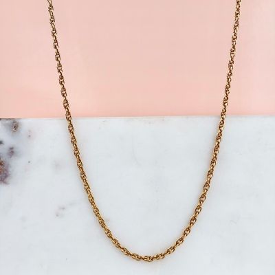 un collier à chaîne en or posé sur une surface en marbre, sur fond rose