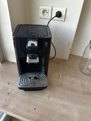 a black coffee maker on a wooden table next to a window