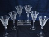 six verres à vin posés sur une table où se trouve une horloge