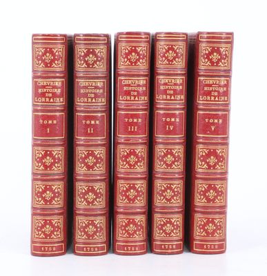 six livres rouges aux tranches dorées sont alignés sur une surface blanche