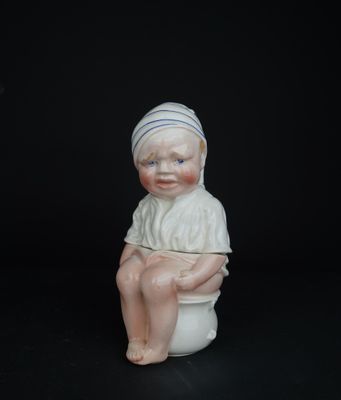 une petite figurine représentant un garçon assis sur des toilettes