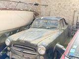 two old cars in a garage with a boat in the background