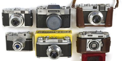 several old cameras are lined up in a row on a white surface
