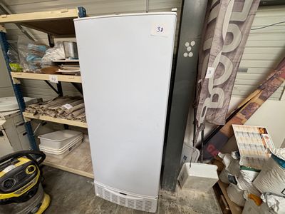 un réfrigérateur blanc dans un garage, à côté d'une étagère où sont rangés d'autres objets
