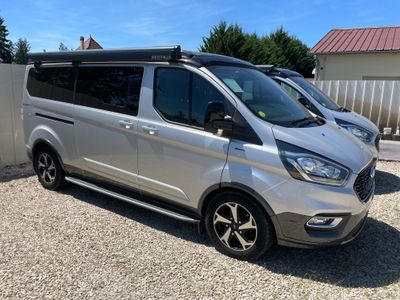 La camionnette argentée est garée sur le gravier, près d'une clôture.