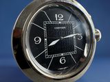 a silver clock with a black face sitting on a table
