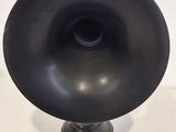 a black vase on a stand on a white surface