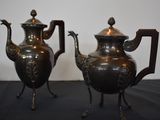 two silver teapots sitting next to each other on a table