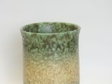a green and brown vase sitting on a white surface