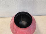 a red vase sitting on a table with a white wall in the background