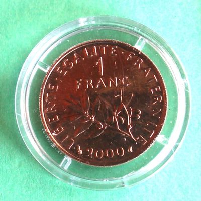 une pièce de monnaie dans un récipient en plastique transparent posé sur une surface verte