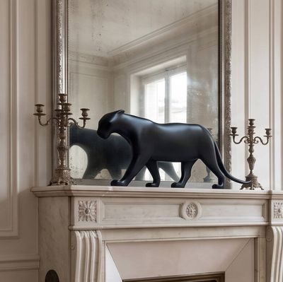 une statue de chat posée sur une cheminée, devant un miroir