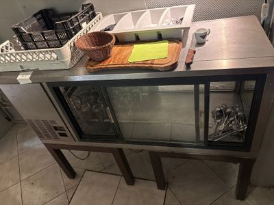 un plan de travail en acier inoxydable muni d'une porte vitrée et d'un panier posé dessus