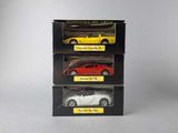 three toy cars are in a black box on a white surface