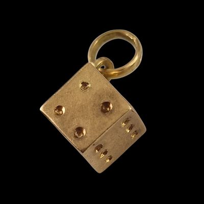 a close up of a gold plated dice charm on a black background
