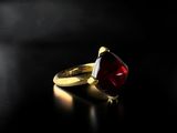 a gold ring with a red stone on a black surface