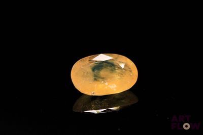 an oval yellow diamond on a reflective surface with a black background