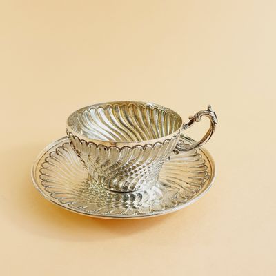 a silver cup and saucer sitting on a saucer