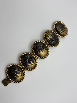 a close up of a gold and black bracelet on a white surface
