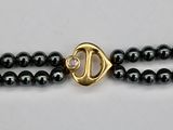 a close up of a black beaded necklace with a gold clasp