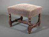 an antique foot stool with a velvet upholstered seat and turned legs