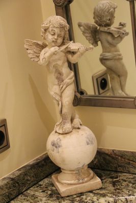 une statue représentant un Cupidon, posée sur un socle devant un miroir