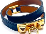 deux bracelets en cuir bleu rehaussés de détails en métal doré sur fond blanc