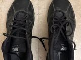 pair of black sneakers with laces on the soles on a tiled floor